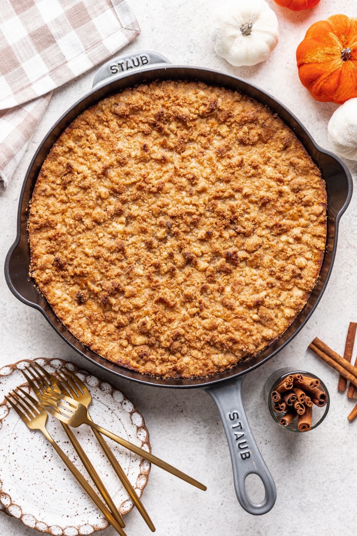 A skillet of pumpkin crisp next to a stack of plates and gold forks.