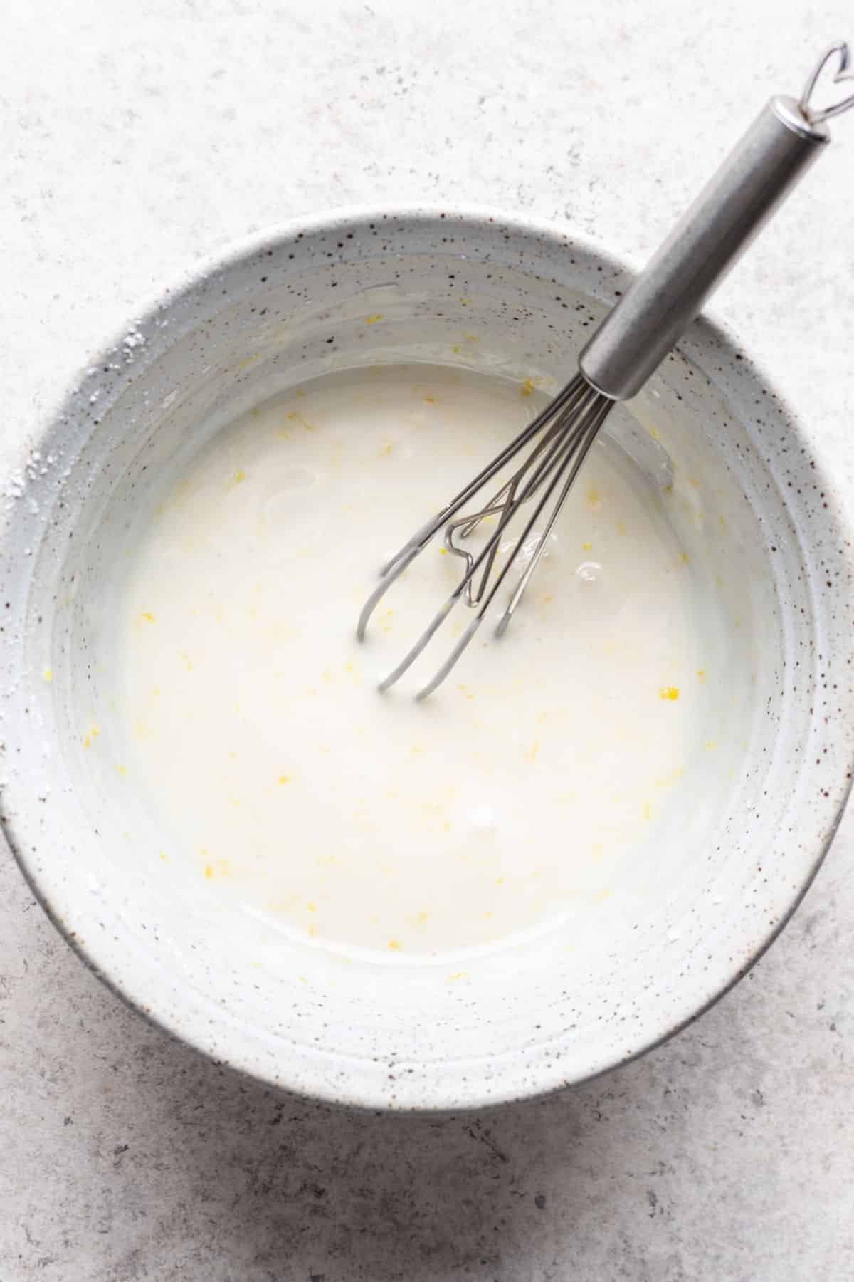 7 up pound cake icing in a white mixing bowl with a whisk in it. 