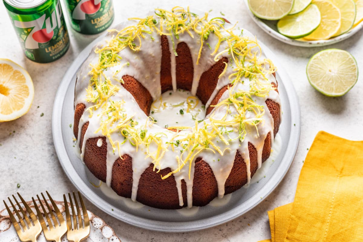 An iced 7UP pound cake on a platter next to a stack of plates and forks. 