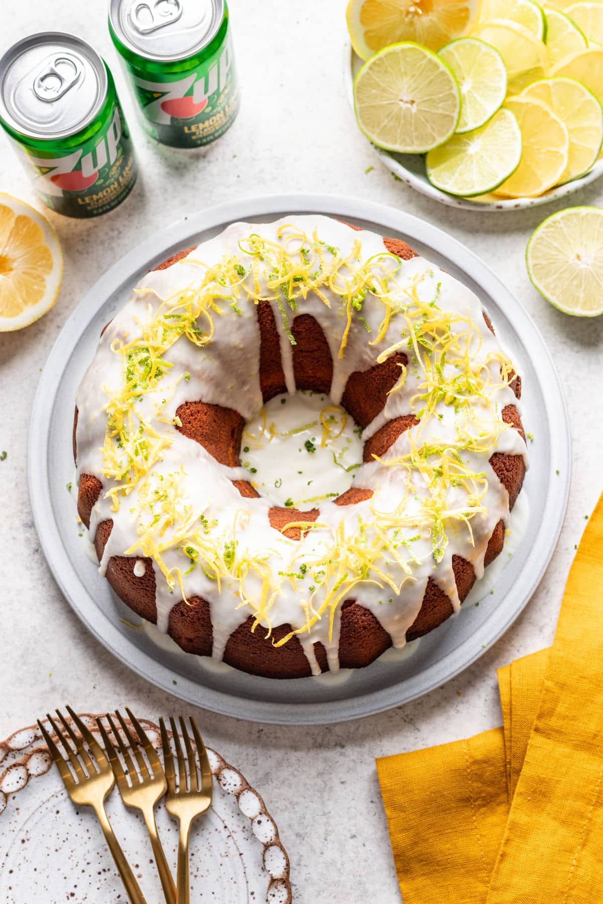 An iced 7 up pound cake on a platter next to sliced lemons and cans of 7 up.