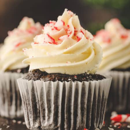 Three chocolate peppermint cupcakes on a wooden cutting board.