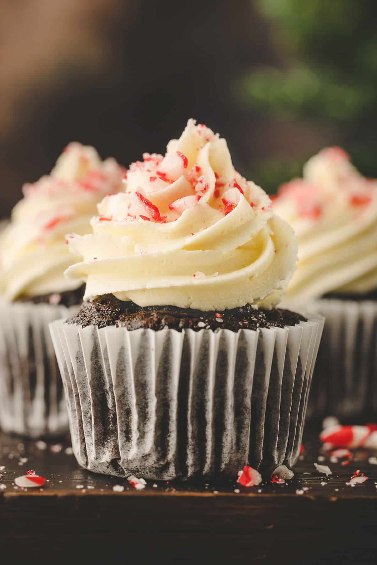 Three chocolate peppermint cupcakes on a wooden cutting board.