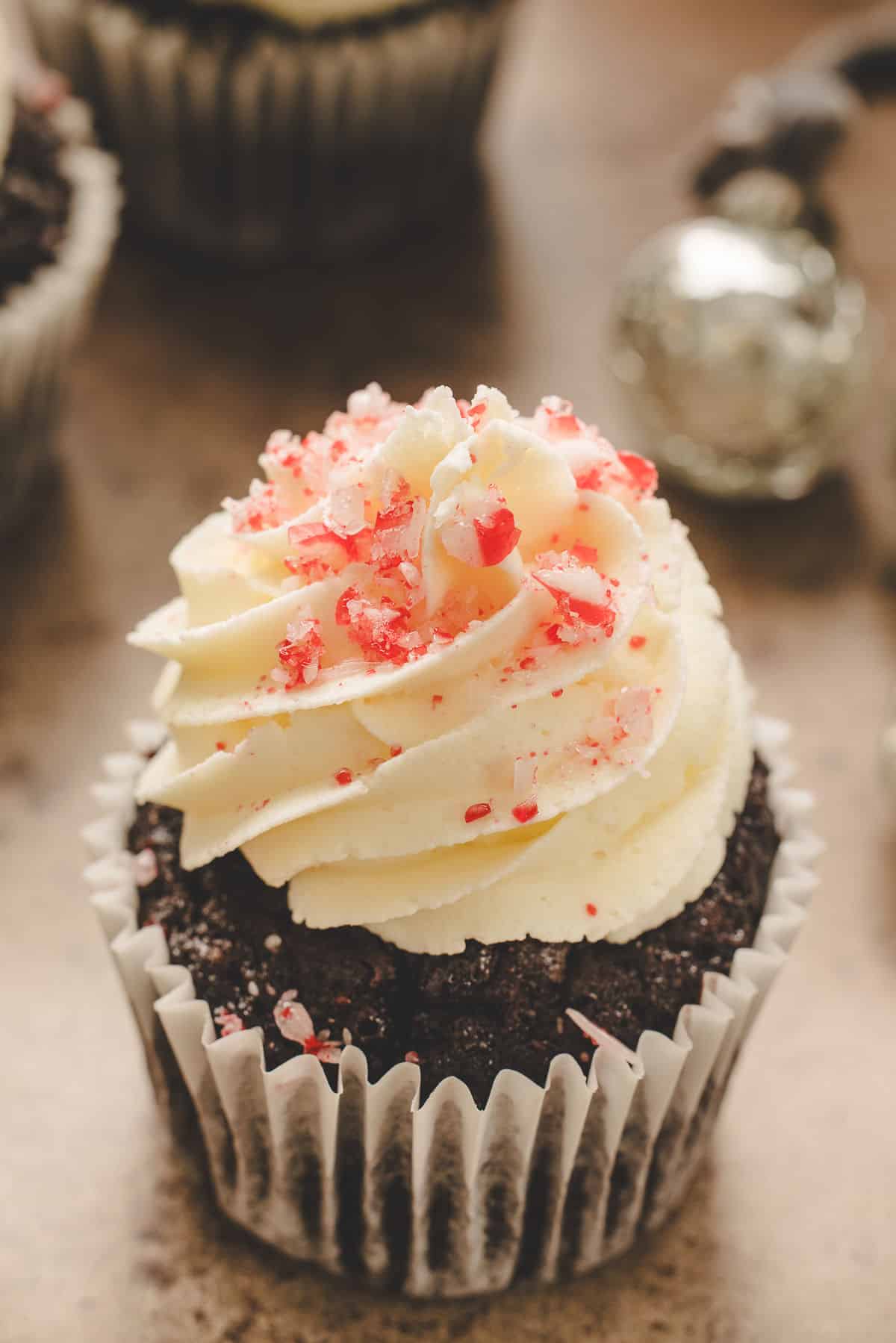 A chocolate peppermint cupcake next to a silver jingle bell. 