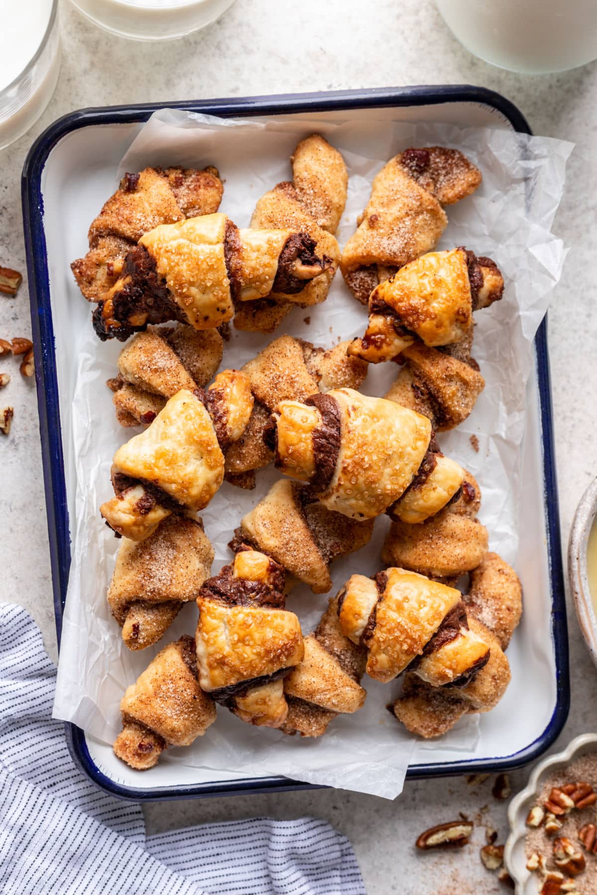 Rugelach au Nutella dans un plateau à pâtisserie tapissé de papier sulfurisé à côté d'un linge de cuisine bleu.