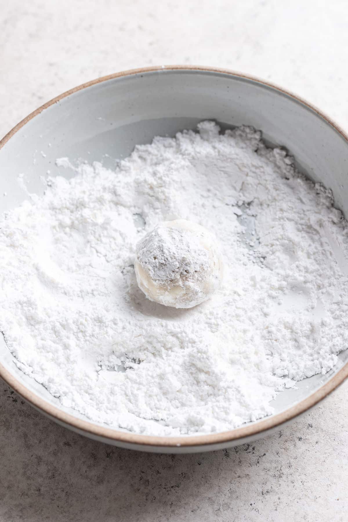 A Mexican wedding cookie rolled in powdered sugar in a dish of powdered sugar. 