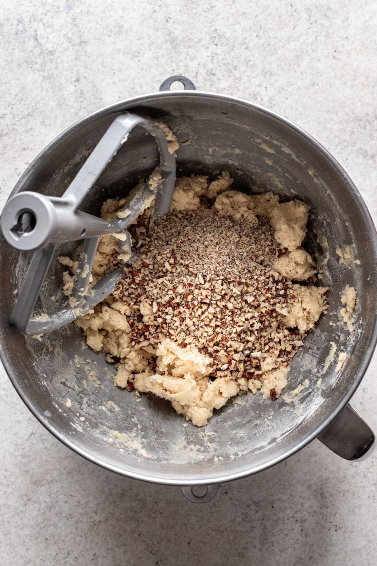 Chopped pecans sitting on top of Mexican wedding cookie dough. 