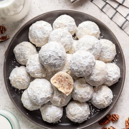 A plate of Mexican wedding cookies with one cookie cut in half on top.