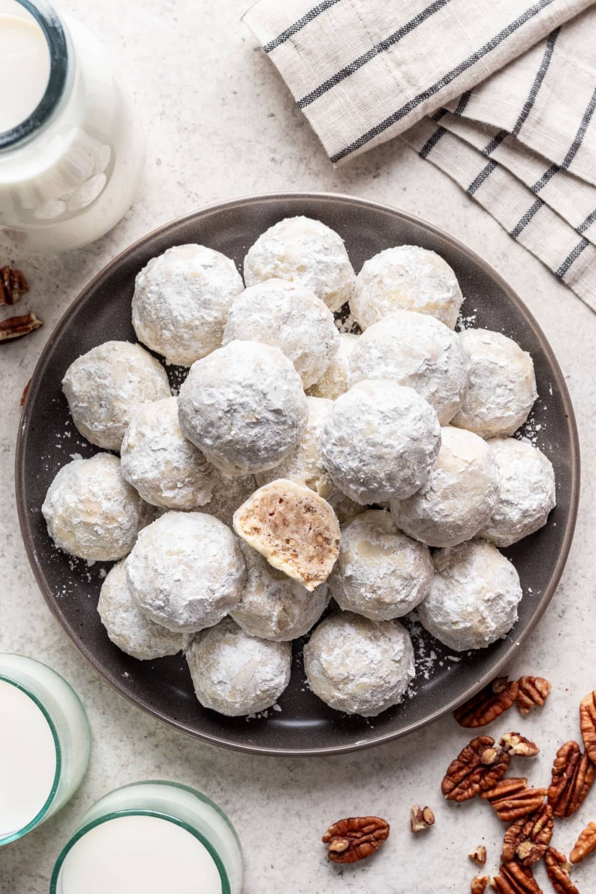 A plate of Mexican wedding cookies with one cookie cut in half on top.