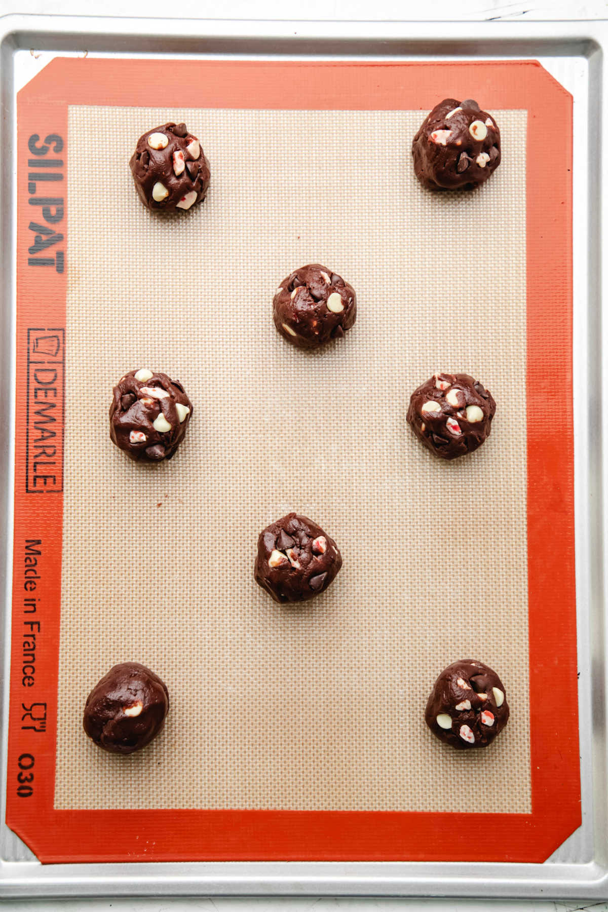 Scoops of peppermint bark cookie dough on a baking sheet. 