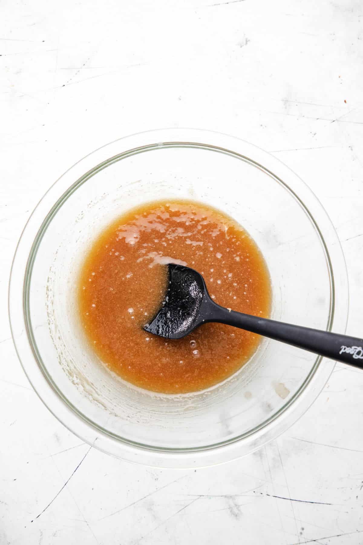 Melted butter and sugars stirred together in a glass mixing bowl. 