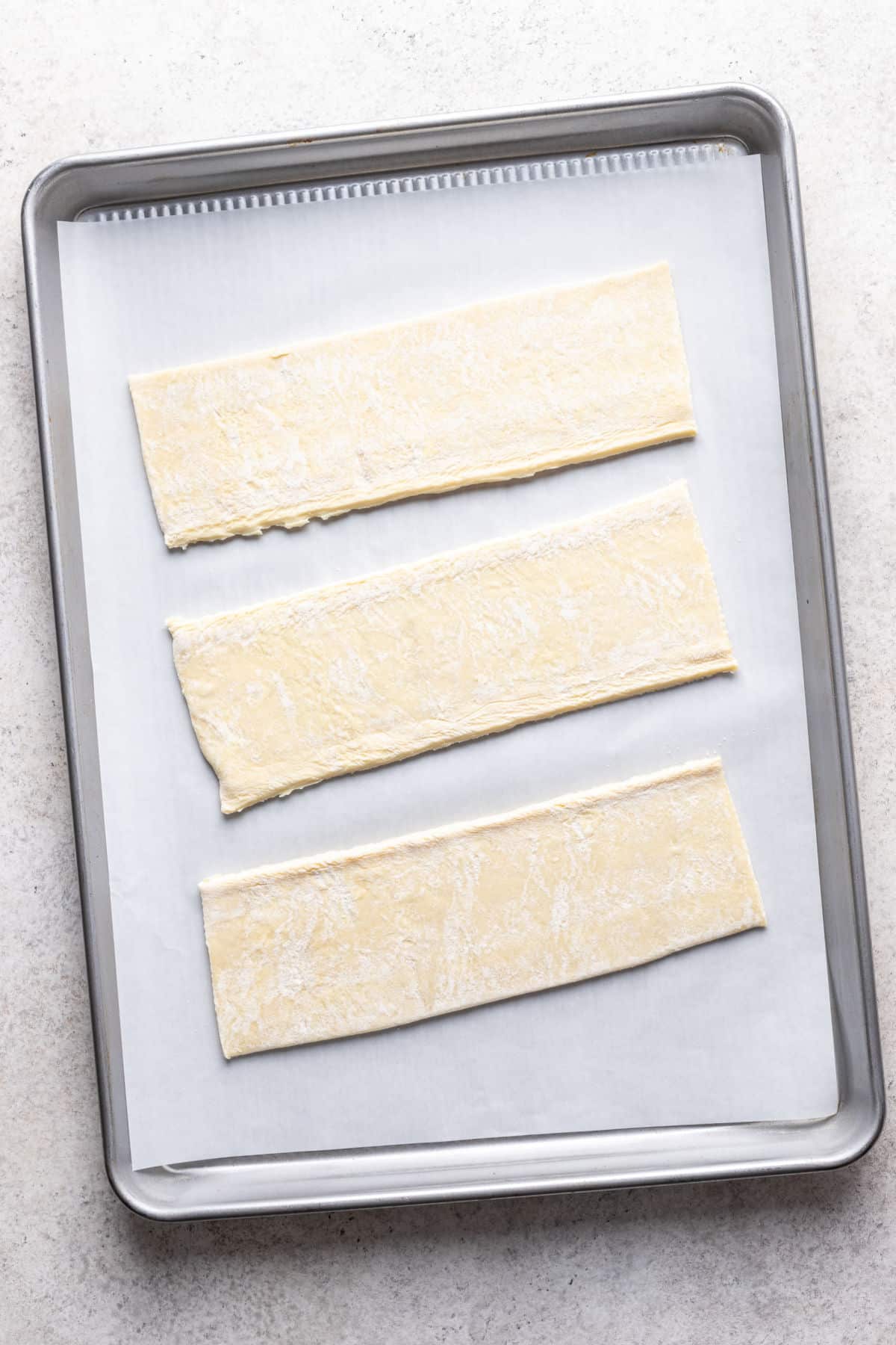 A piece of puff pastry dough cut into three long strips. 