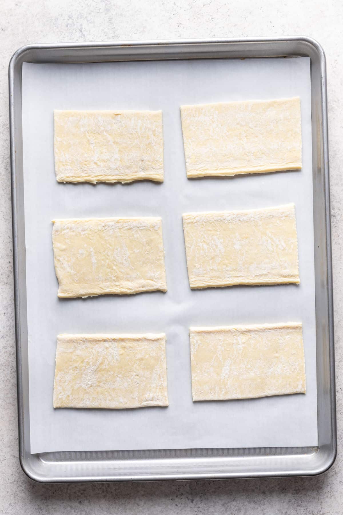 Six pieces of puff pastry dough on a baking sheet. 