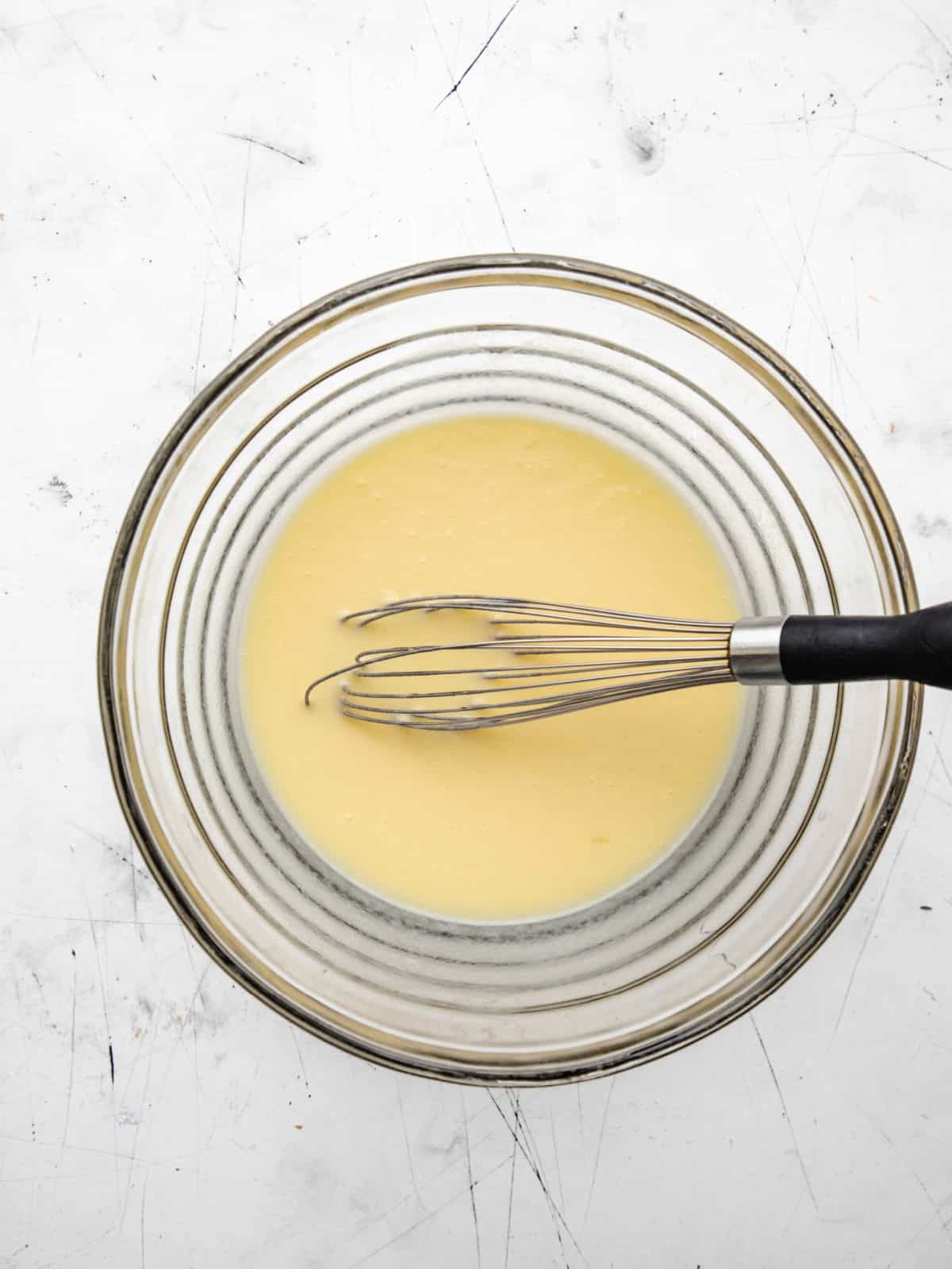 Wet ingredients for honey cornbread muffins in a glass mixing bowl. 