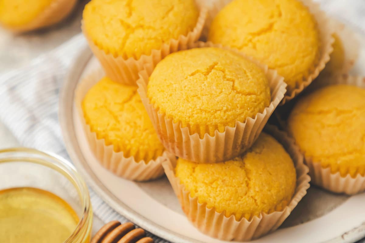 Stacked honey cornbread muffins on a white plate. 