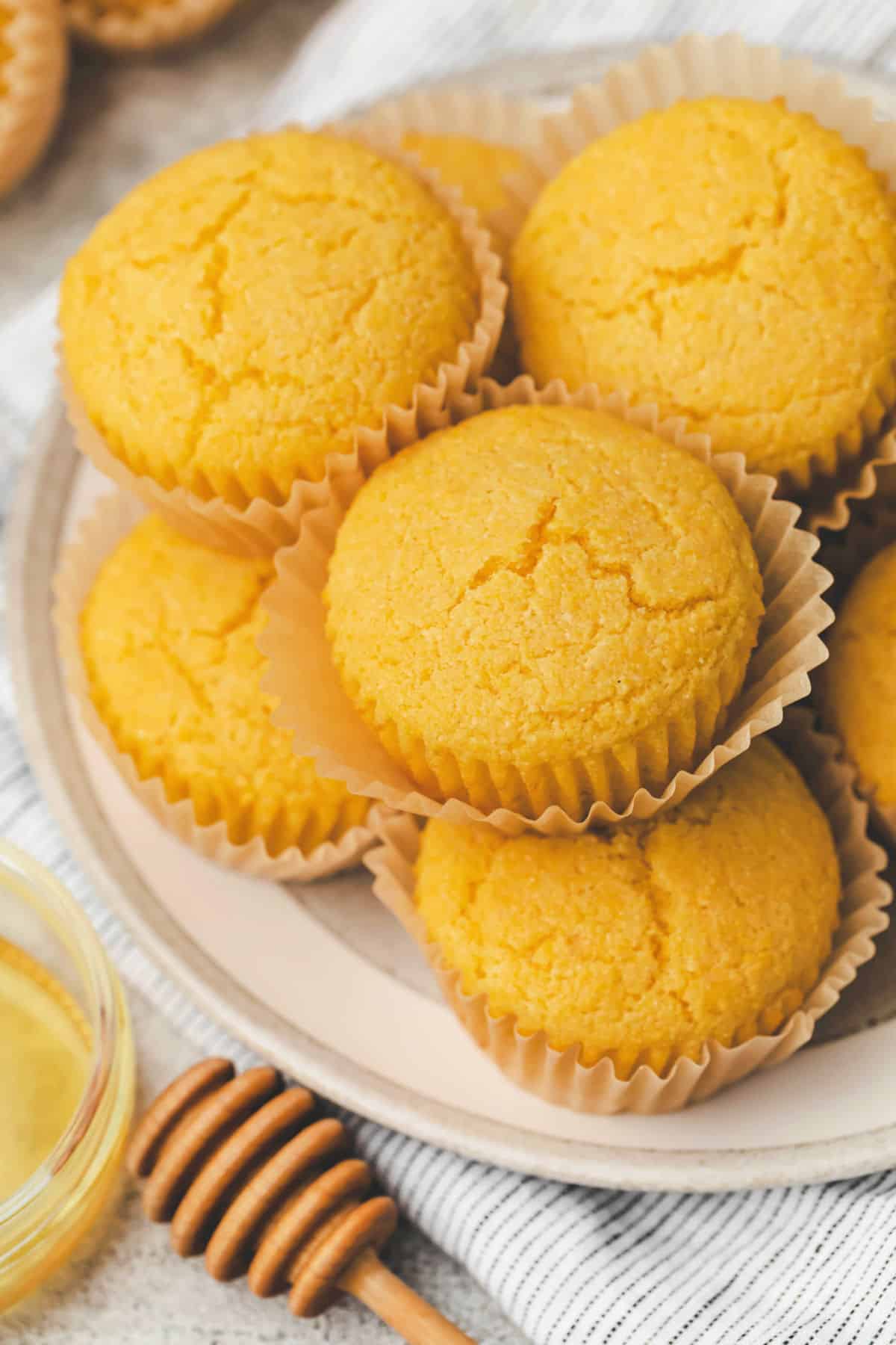 Honey cornbread muffins stacked on a plate next to a dish of honey.