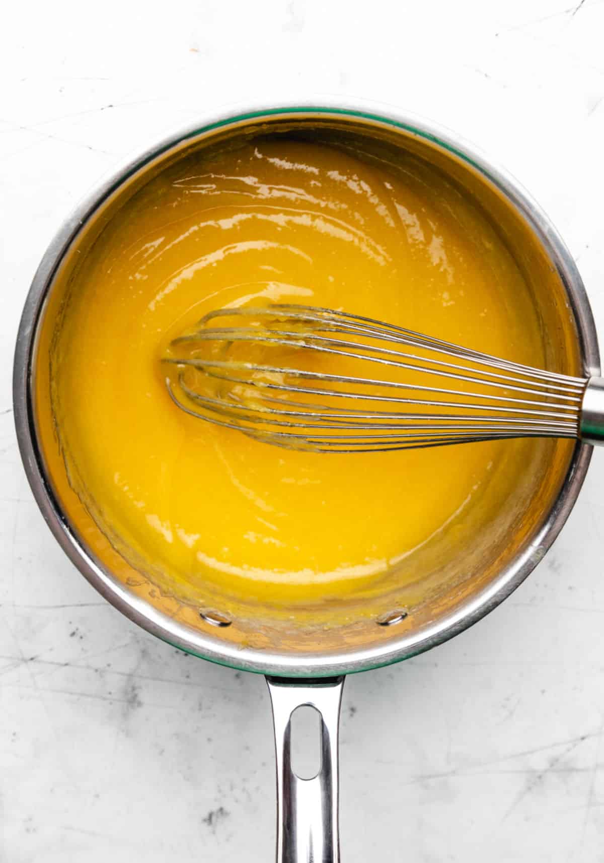 Cooked lemon curd with a whisk in it in a saucepan.