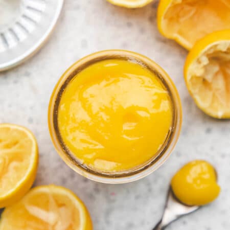 A glass jar of lemon curd next to a spoon of lemon curd.