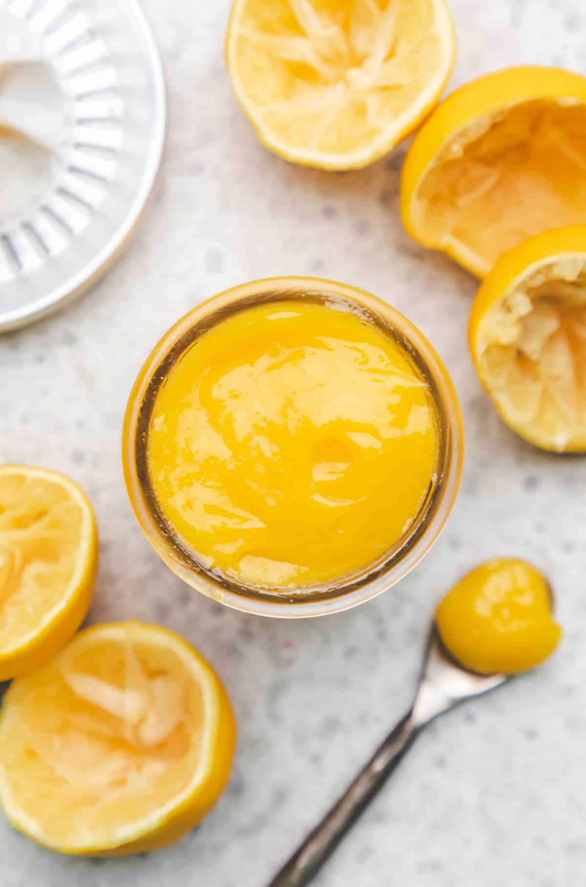 A glass jar of lemon curd next to a spoon of lemon curd. 