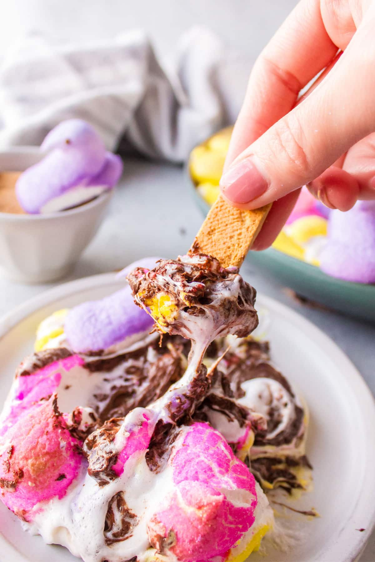 A hand holding a graham cracker dipping into Peeps s'mores dip. 