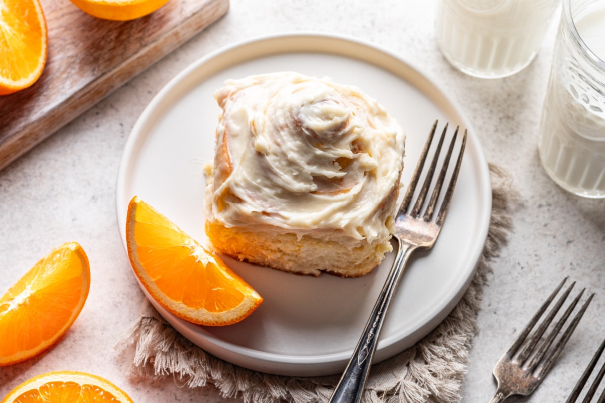 Une brioche à l'orange dans une assiette avec une fourchette et un quartier d'orange à côté.